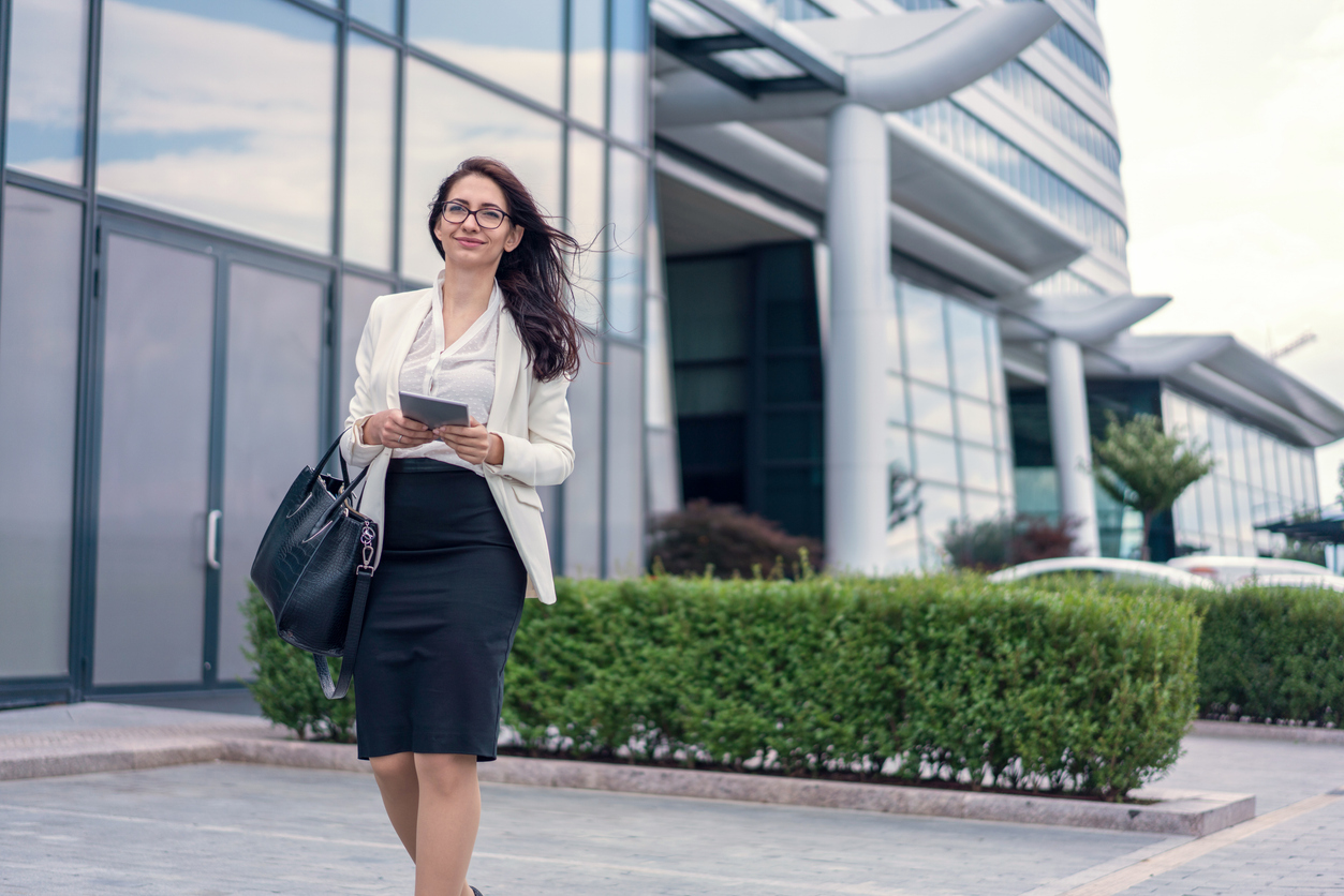 A health care executive holding a tablet walks outside a hospital building.
